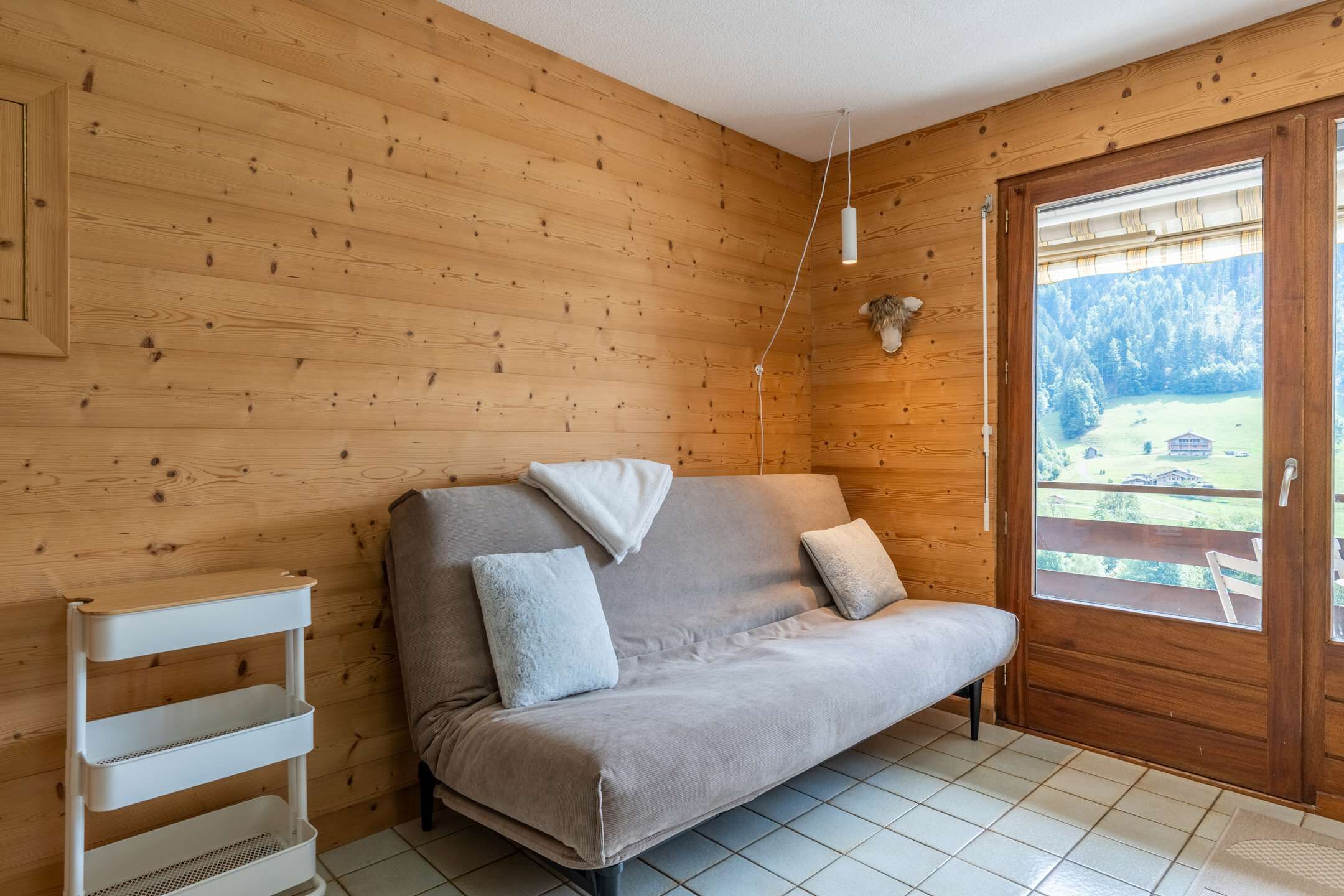 Ein Holzinnenraum mit einer Couch, einem weißen Regalsystem und einer Tür, die zu einem Außenbereich führt.