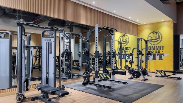 A gym with various exercise equipment, including weight machines and free weights, arranged on a wooden floor with a large mirror and motivational wall art. - Elegant Palm Retreat w Iconic Sea Marina Vws (Dubai)
