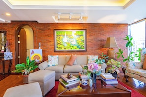 A living room with a brick wall, a sofa, a coffee table with books and a vase, and a painting above the sofa.