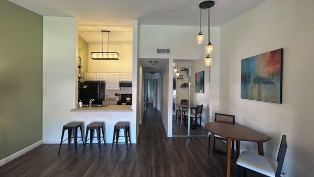 A modern kitchen with white cabinets, a black refrigerator, and a built-in oven. There is a dining area with a wooden table and four chairs.