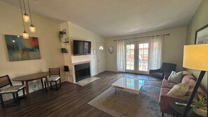 A living room with a fireplace, a flat-screen TV, a dining table with chairs, a sofa, and a coffee table.