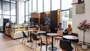 Un café moderno con una vitrina de pastelería, arreglos de asientos y un amplio ventanal.