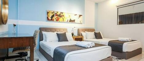 A hotel room with two beds, a desk, a chair, a large mirror, and artwork on the wall.
