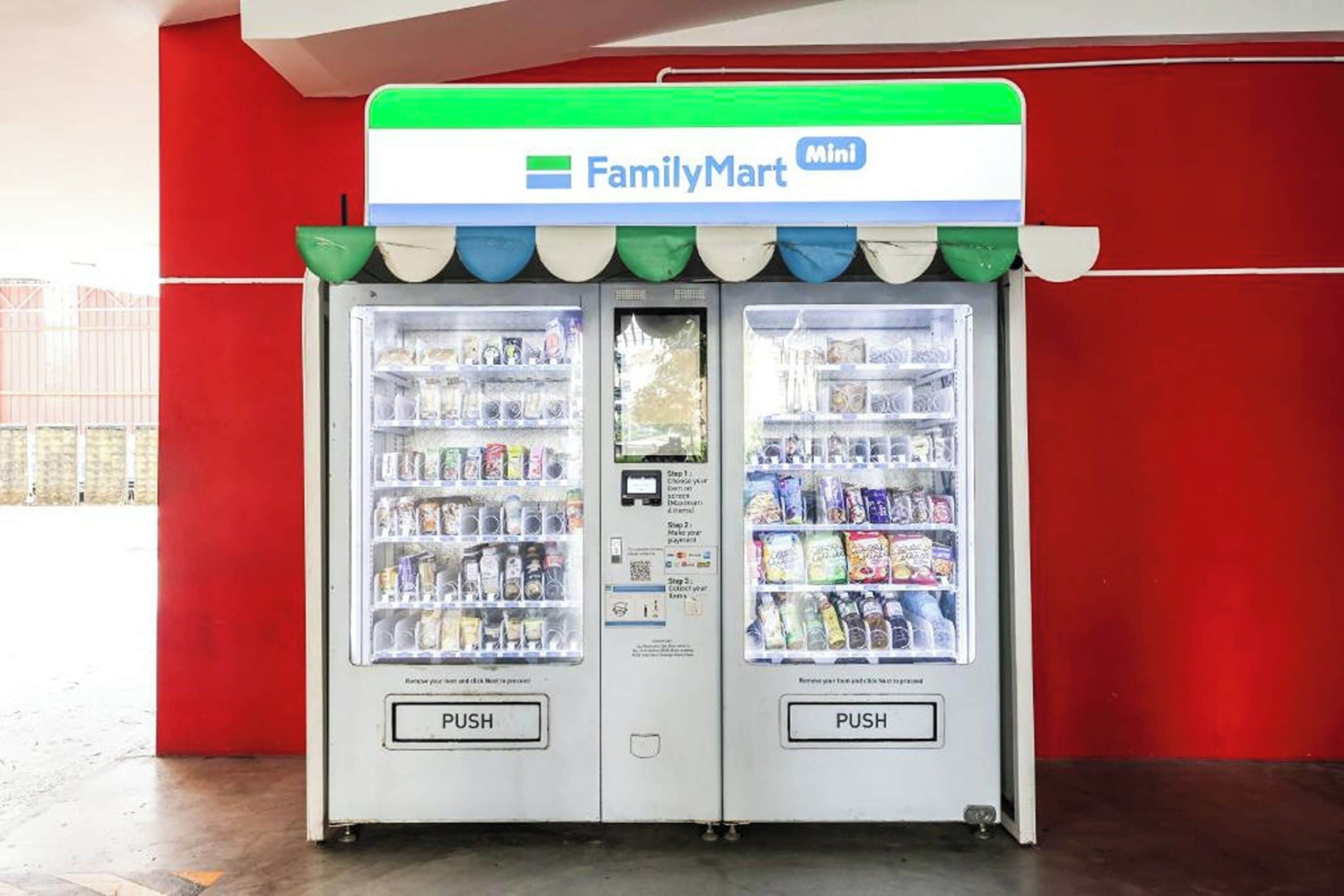 Una máquina expendedora de FamilyMart Mini con dos botones pulsadores, ubicada frente a una pared roja.