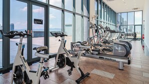 Un gimnasio con diversos equipos de ejercicio, amplias ventanas y vistas a la ciudad.