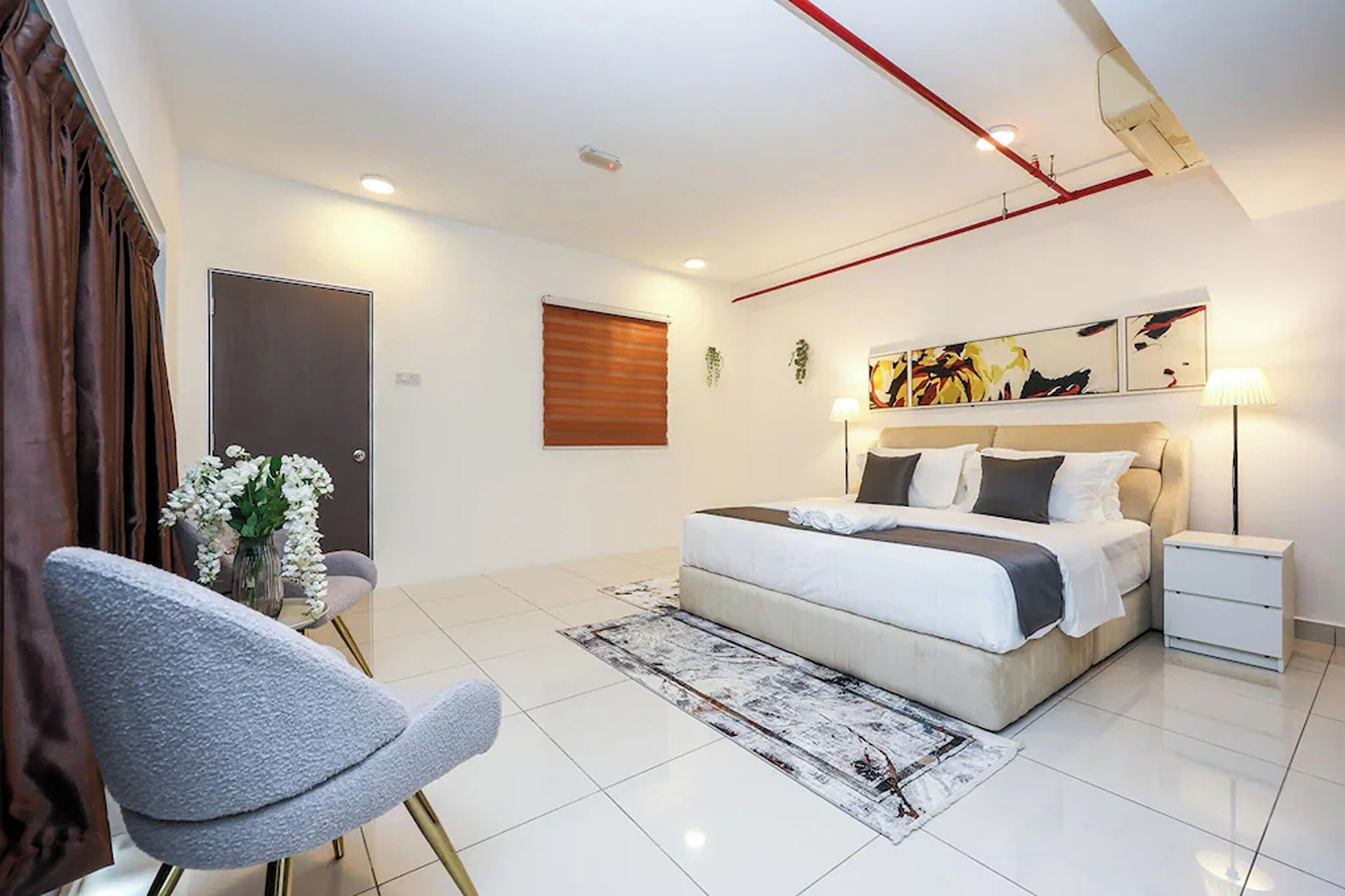 Une chambre à coucher moderne avec un lit, des tables de chevet, une chaise, un tapis et des œuvres d’art accrochées au mur.
