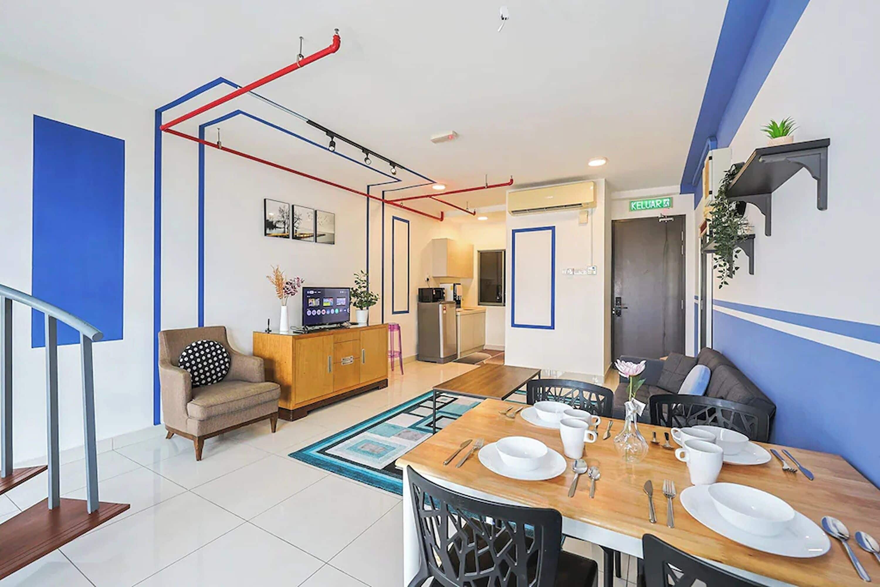 A modern hotel room with a dining area, kitchenette, and a staircase.