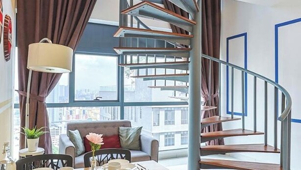 Un interior moderno con una escalera espiral, un área de comedor con una mesa preparada para cuatro personas y un sofá con cojines.