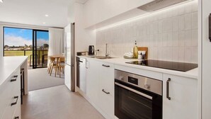 A modern kitchen with white cabinetry, a built-in oven, and a large window overlooking a balcony. - Relaxing Home in Waihi Beach (#B2) (Waihi Beach)