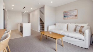 A modern living room with a white sofa, a wooden coffee table, and a painting on the wall. - Relaxing Home in Waihi Beach (#B2) (Waihi Beach)
