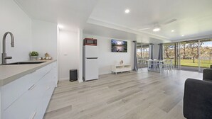 A modern kitchen with a built-in stove, a microwave, and a sink. There is a dining area with a table and chairs, and a large window offering a view of the outdoors. - Absolute Waterfront Bliss – Pet Friendly, Seperate living areas, Family Shack. (Pellaring Flat)