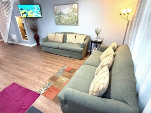 A living room with a green sofa, a wooden floor, a flat-screen TV, and a painting on the wall. -  3-bedroom 1 bath. House with off street parking and large fenced in backyard. (Wilmington)