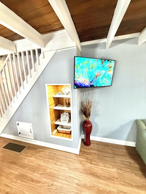 A room with a wooden staircase, a mounted television, and a built-in shelving unit with decorative items.