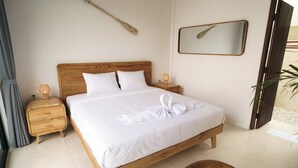 Een net opgemaakt bed met een houten hoofdbord, een nachtkastje met een lamp en een spiegel aan de muur.