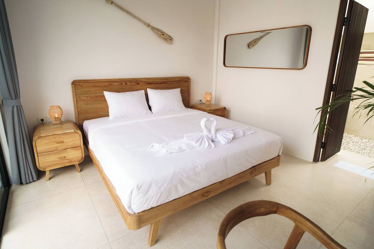 A neatly made bed with a wooden headboard, a bedside table with a lamp, and a mirror on the wall.