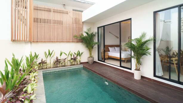 Een modern zwembadgedeelte met een houten terras, een slaapkamer met glazen wanden, en verschillende potplanten.