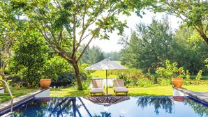 An infinity pool with two lounge chairs and an umbrella, surrounded by lush greenery and trees. - Danang private pool villa by Esea43 (Da Nang)