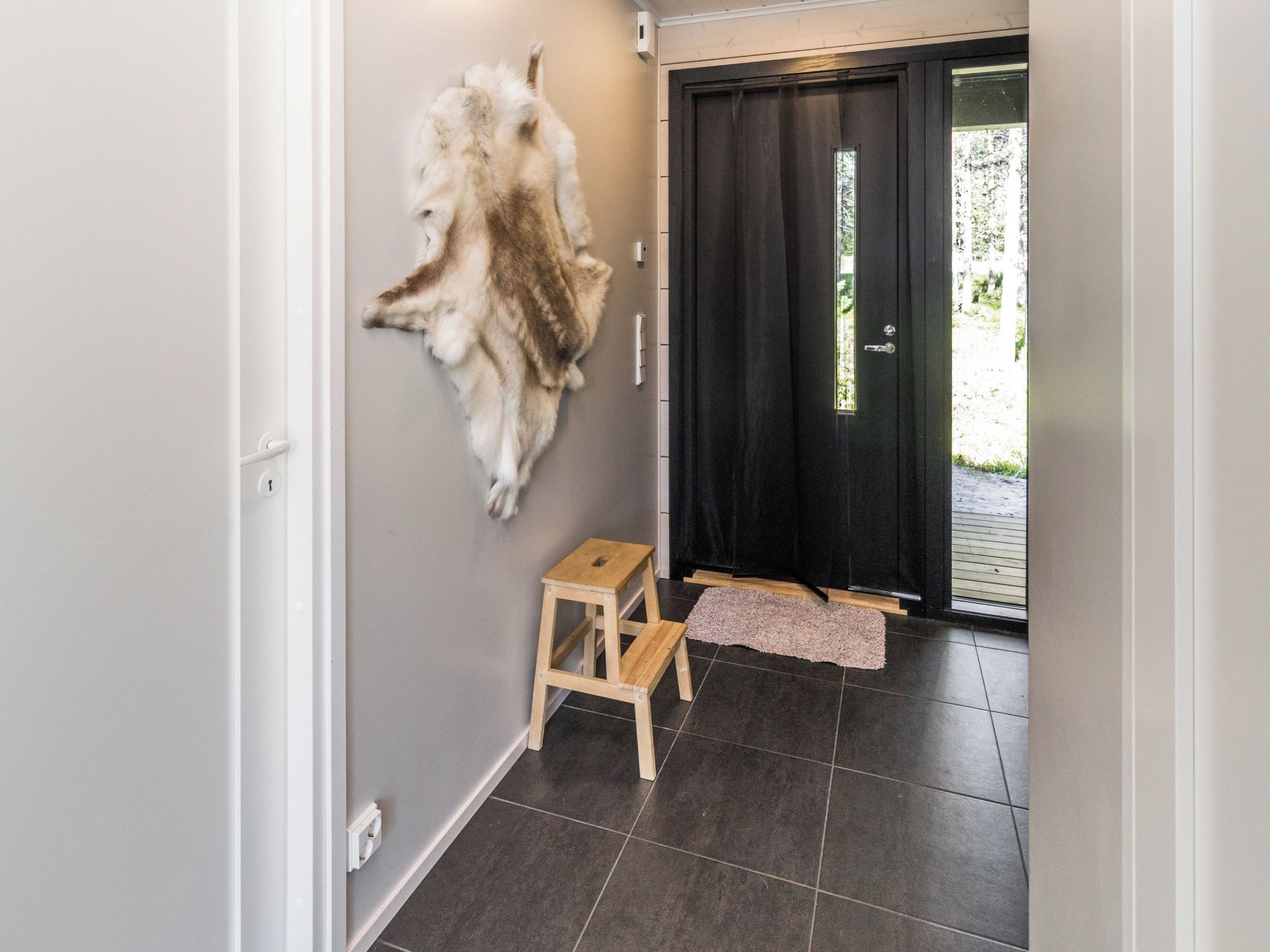 A hallway with a fur coat on the wall, a wooden stool, and a black door.