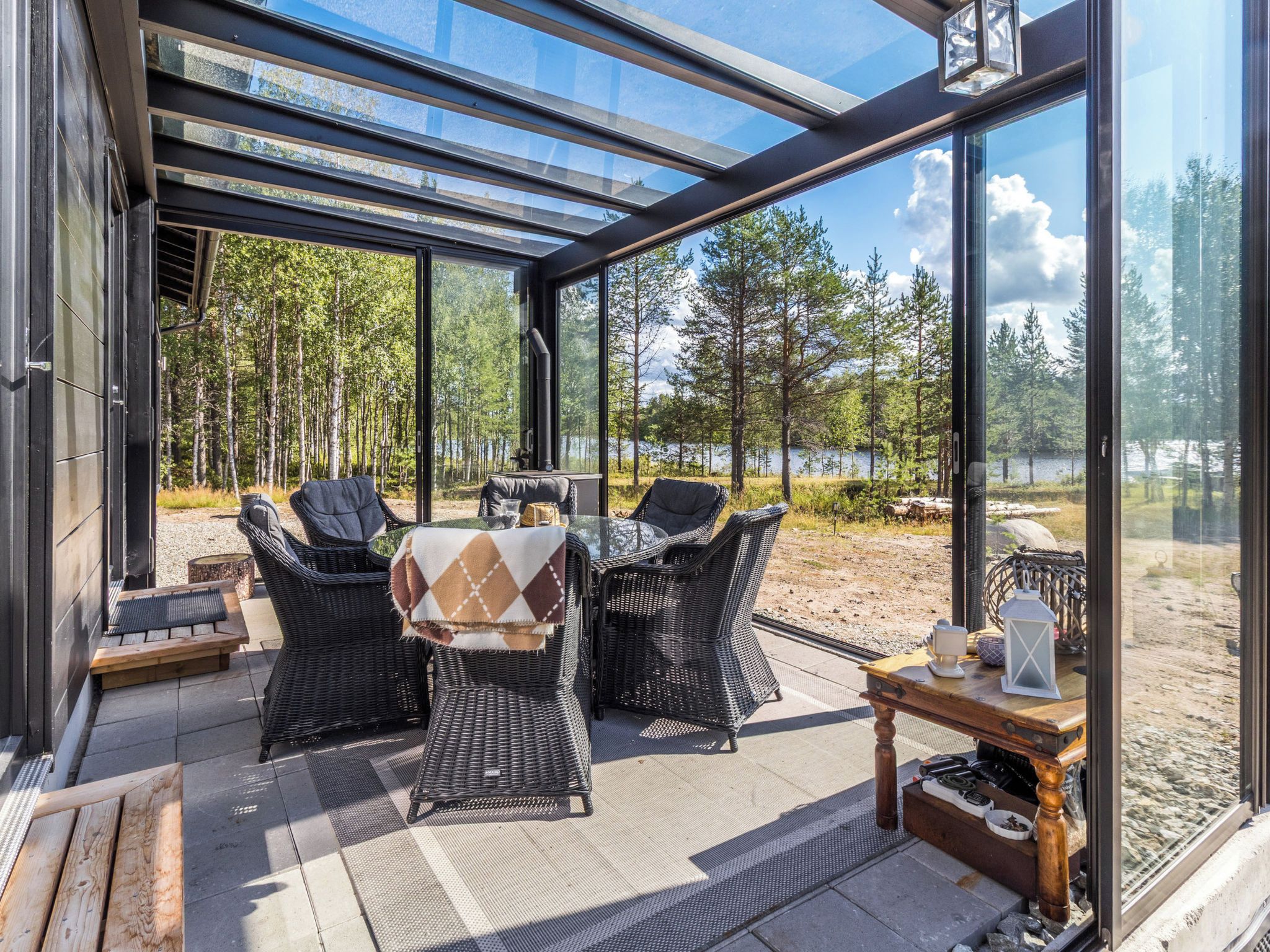 Lasiseinöin varustettu terassi, jossa on ulkokalusteita, pöytä sekä näkymä metsään ja järvelle.