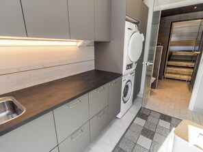 A modern kitchen with a built-in washing machine, grey cabinets, and a stainless steel sink.