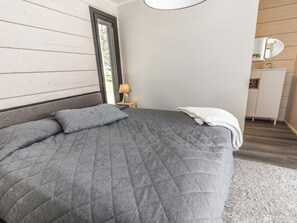 A bedroom with a large bed, a bedside table with a lamp, a dresser, and a mirror on the wall.