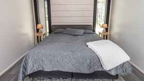 A bedroom with a large bed, two bedside tables with lamps, a grey quilted bedspread, and a white throw blanket.