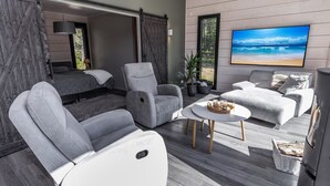 A modern living room with a large TV, grey sofas, a coffee table, and a sliding door leading to a bedroom.