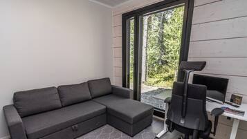 A modern room with a sectional sofa, a desk with a computer, and a view of a forest through a sliding door.