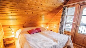 Un dormitorio de cabaña de madera acogedor, con una cama, una mesita de noche, una lámpara y una ventana con cortinas.