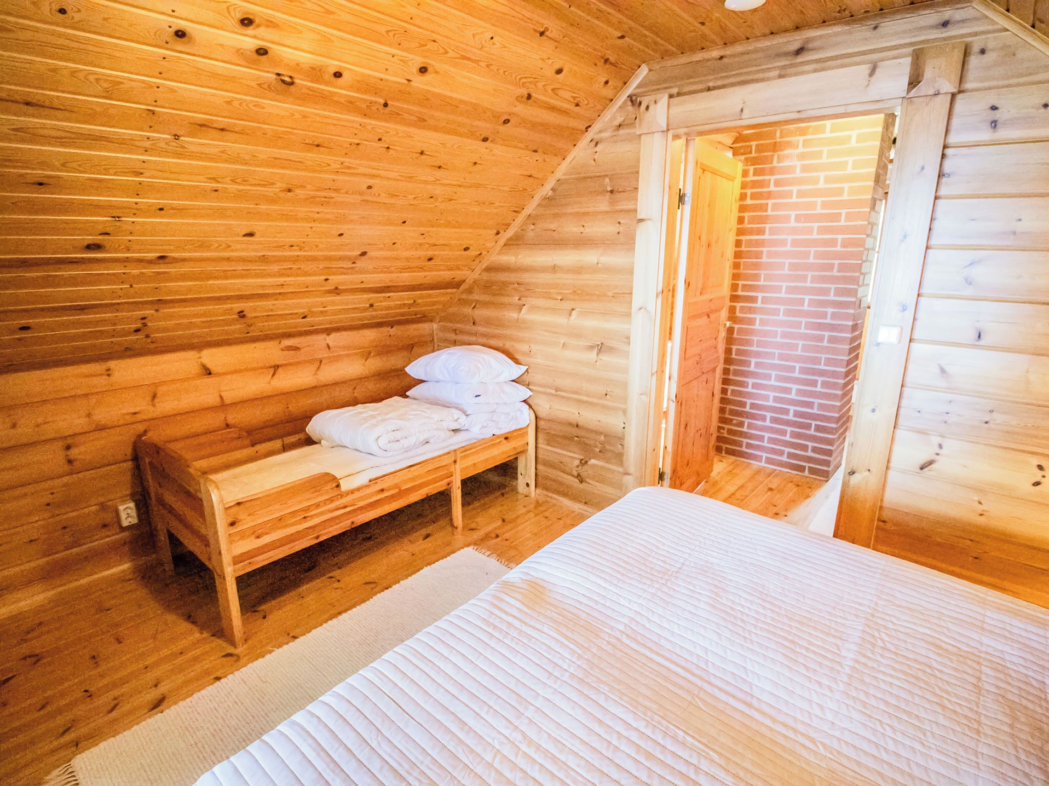 A wooden cabin room with a bed, a bench, and a fireplace.