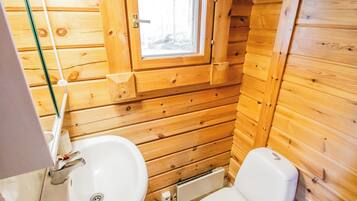 Bany d'una petita cabana de fusta, amb finestra, un lavabo i un vàter.