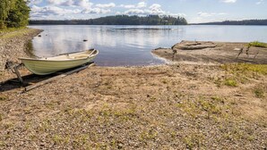 En båt ligger vid en grusstrand på en stilla sjö, med en skogbeklädd ö i bakgrunden.