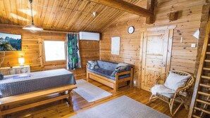 En mysig stuga med träinredning, en soffa, en fåtölj, en säng och ett skrivbord med en lampa.
