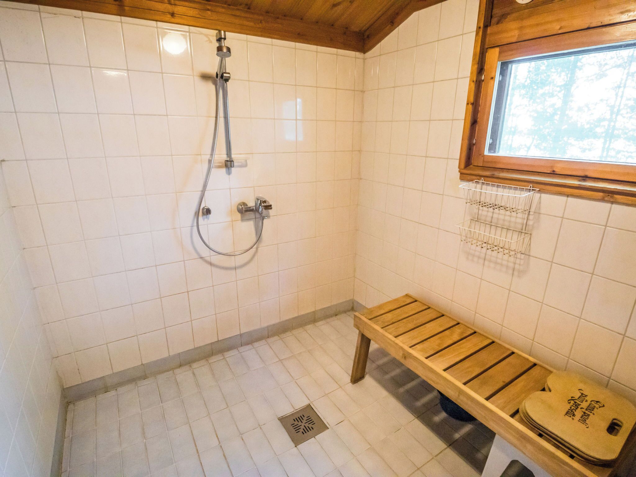 A small, tiled shower area with a wooden bench and a window.