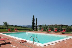 A rectangular swimming pool with clear blue water, surrounded by red lounge chairs and a covered seating area.