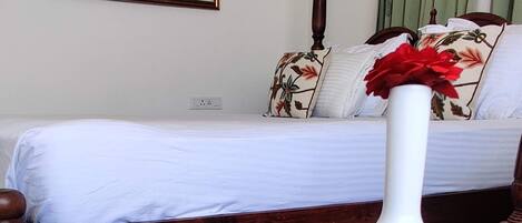 A room with a bed, a white vase with red flowers, and scattered orange petals on the floor.