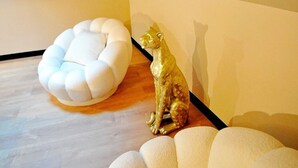 A room with a white, circular, cushioned seating area and a golden statue of a cat.