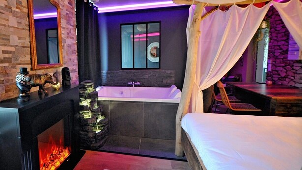 A modern bedroom with a large bed, a fireplace, a bathtub, and a stone wall.