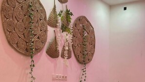 A room with three cushioned chairs, a wooden ladder with potted plants, and two large woven wall decorations. - Modern vacation apartment with washing machine and king-size bed (Lomé kpogan)