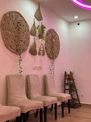 A room with three cushioned chairs, a wooden ladder with potted plants, and two large woven wall decorations. - Modern vacation apartment with washing machine and king-size bed (Lomé kpogan)