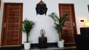 A reception area with two potted plants, a Buddha head sculpture, and a small table with a statue. - Cozy and Tranquil Nest ( With wifi and Homely Care ) (Greater Noida)