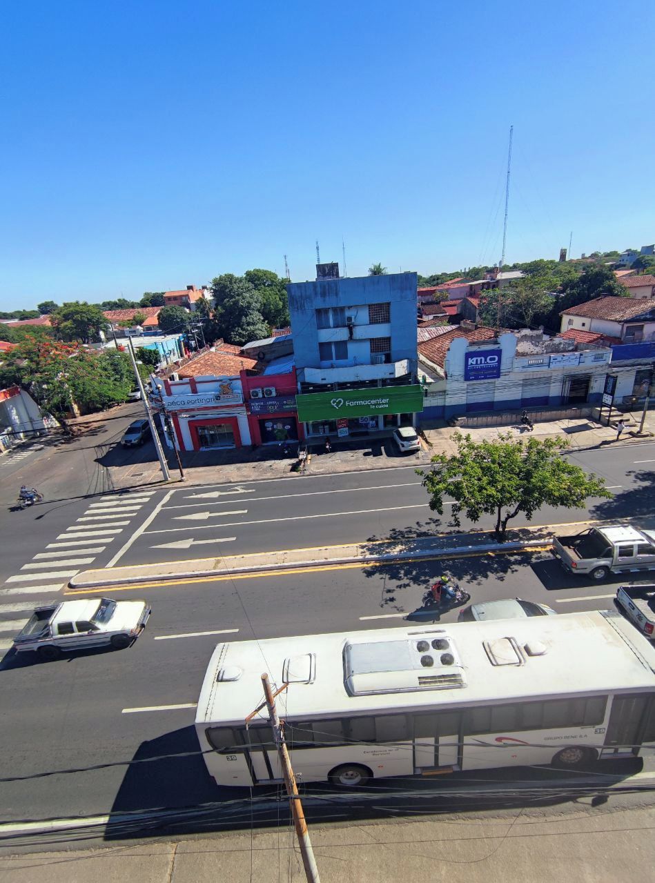 Une vue de rue avec un arrêt de bus, une pharmacie et un bâtiment sur lequel on peut lire l’inscription « Farmcenter ».
