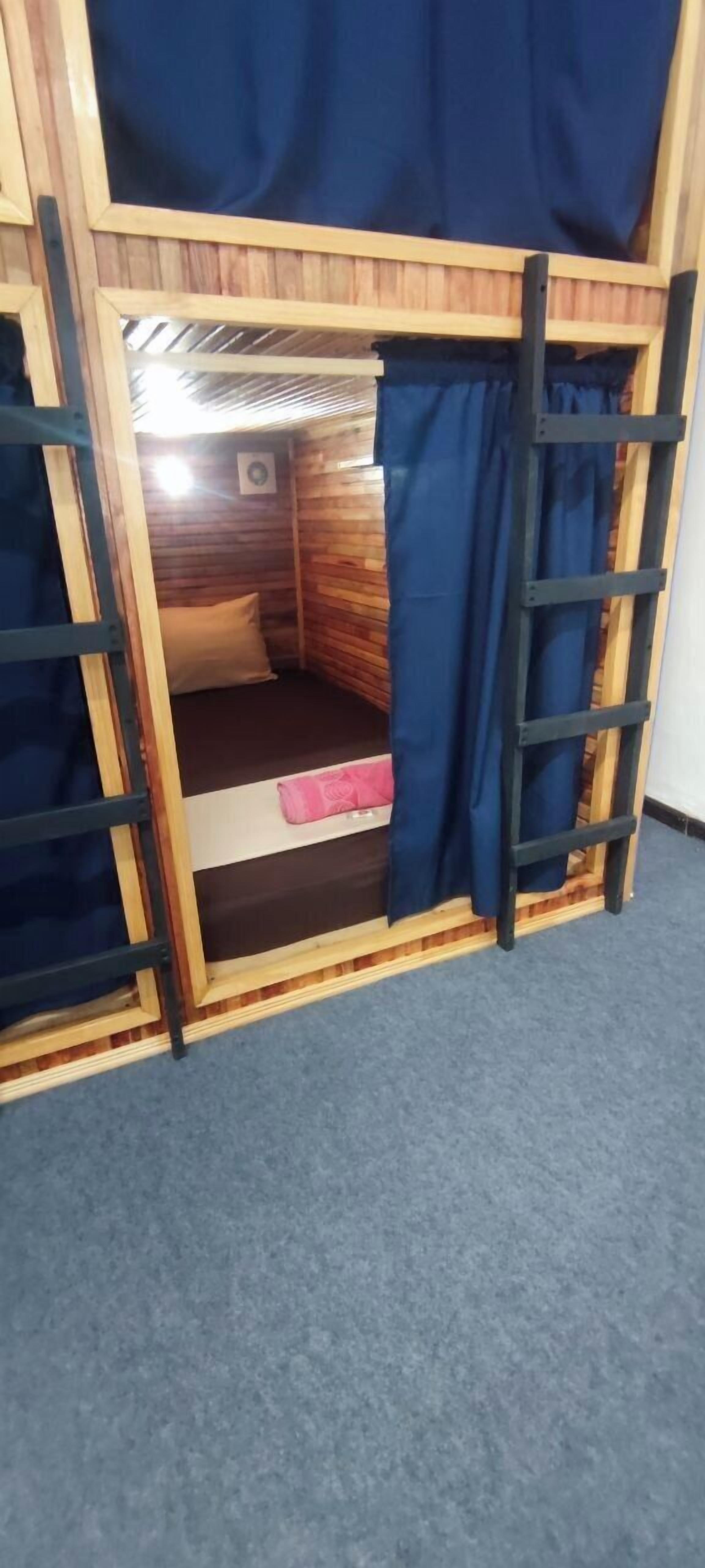 Una cama litera con estructura de madera, una cortina azul y una escalera.