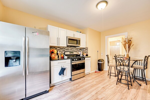 A modern kitchen with stainless steel appliances, white cabinets, and a dining area with metal chairs.