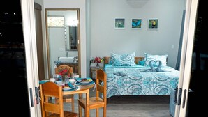 Ein Schlafzimmer mit einem Bett, zwei Stühlen, einem Tisch mit Blumenvase und einem Spiegel.