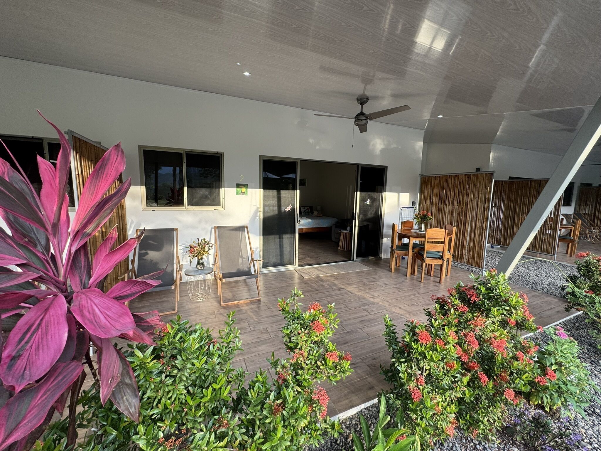 Un espacio interior moderno con un ventilador de techo, una zona de comedor con mesa y sillas, y una planta grande en maceta.