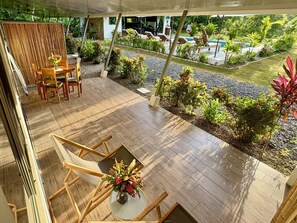 Ein überdachter Außenbereich mit Holzterrasse, einem Tisch mit Stühlen und einem kleinen Garten mit verschiedenen Pflanzen und Blumen.