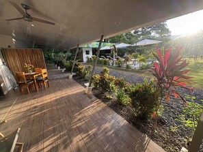 Ein überdachter Außenbereich mit Holzdeck, einem Tisch mit Stühlen und einem Deckenventilator.