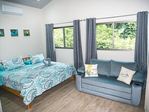 Ein Schlafzimmer mit Bett, Sofa, einem Fenster mit Vorhängen und einer Wand-Klimaanlage.