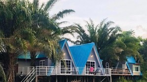 Une maison de plain-pied à deux étages, avec un toit bleu, entourée de palmiers.